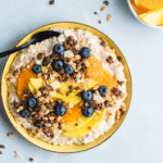 Skål med havregrynsgröt med keso toppad med mango, apelsin, blåbär och granola