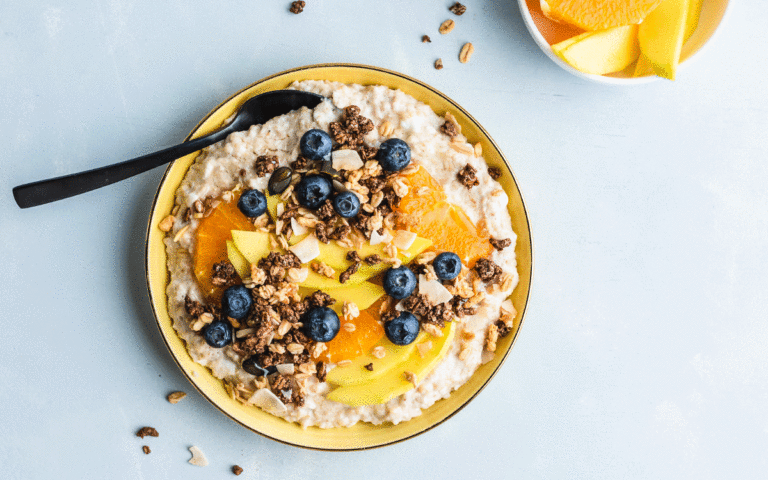 Skål med havregrynsgröt med keso toppad med mango, apelsin, blåbär och granola