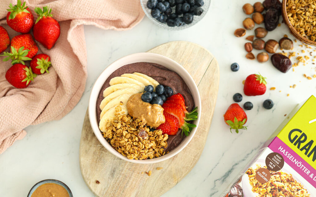Acaibowl toppat med Paulúns Granola Hasselnötter & Dadlar, skivad banan, jordgubbar, blåbär och jordnötssmör.