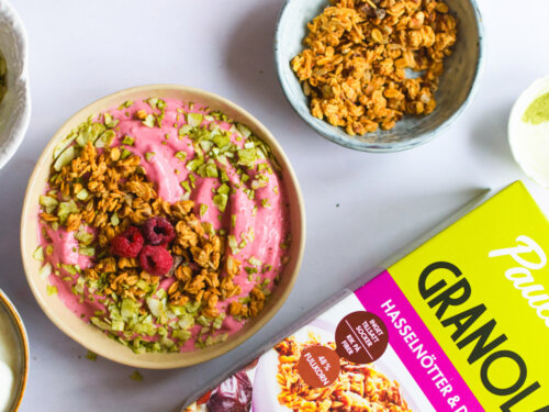 Skål med frozen yoghurt toppad med Pauluns Granola Hasselnötter & Dadlar, matchapulver och hallon.